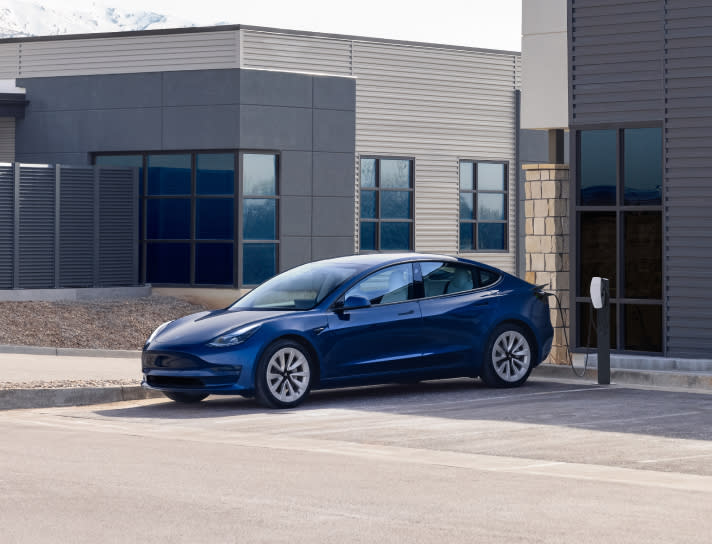 A blue Model 3 charging at a Wall Connector surrounded by industrial buildings