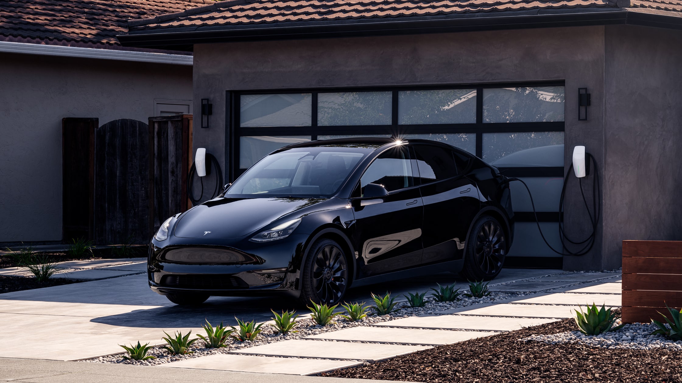 Black Model Y charging with a Wall Connector in front of a residential garage