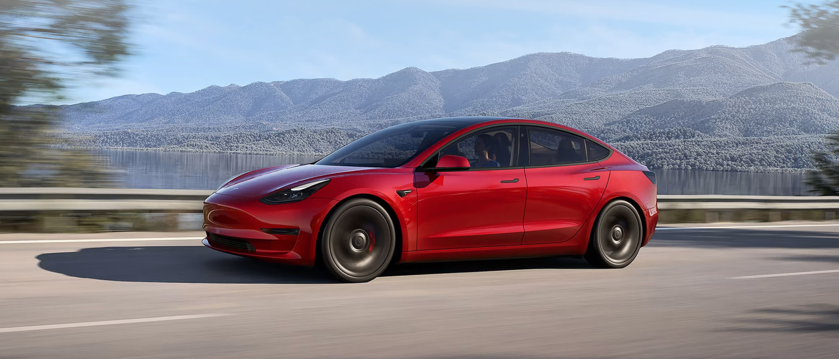 Red Model 3 driving on mountainous road