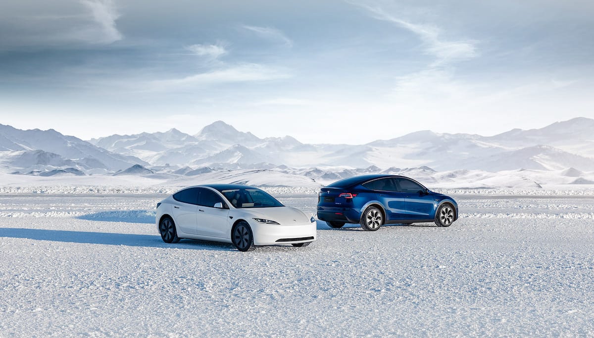 A white Model 3 and a blue Model Y parked on a snowy plain in front of snow-covered mountains