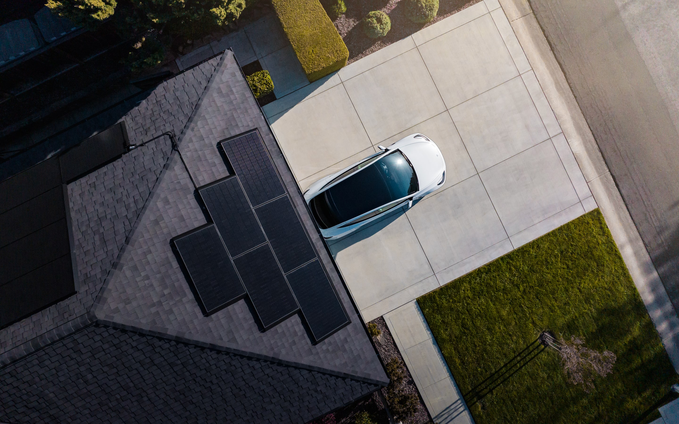 Aerial view of a home with solar panels on a roof with a white Tesla vehicle parked in the driveway
